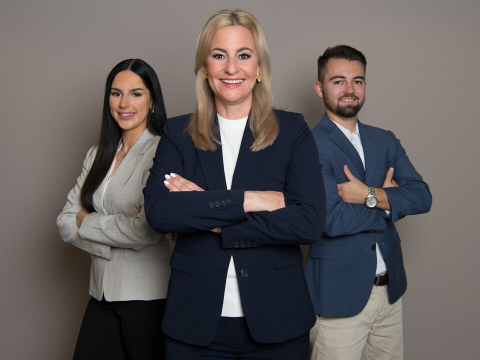 Drei Personen in Businesskleidung lächeln freundlich.